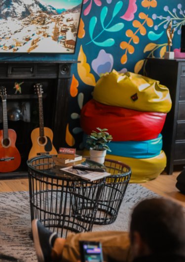 Book Now & Pay Later Living room with some guitars, colourful bean-bags, a guest using their mobile and watching TV at Gardiner House Hostel in Dublin