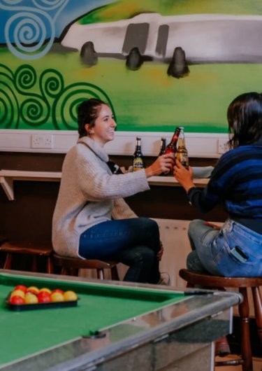 Weekly Deal Two friends cheering beers in a living room with a snooker/pool and chatting